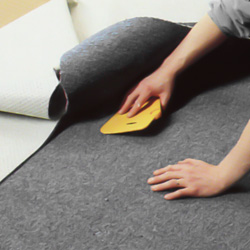 Pressar ut bubblor och veck i mattan med en spackelspade av plast